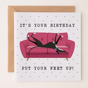 May include: Birthday card with a cartoon dog on a pink sofa. The text above the sofa reads "IT'S YOUR BIRTHDAY" and below it, "PUT YOUR FEET UP!". The background is white with small grey polka dots. The card is in a brown envelope.