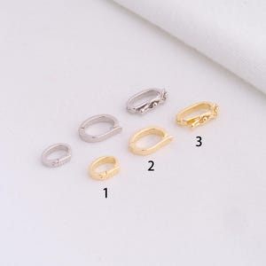 May include: A collection of six small, oval-shaped jewelry clasps in silver and gold tones. The clasps are shown in various sizes and designs, with some featuring decorative elements.