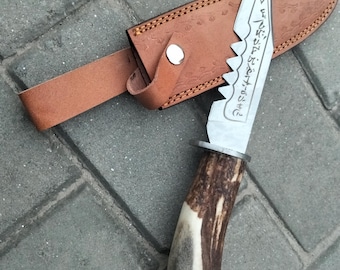 May include: A hunting knife with a serrated blade and a handle made of antler material. The knife is in a brown leather sheath with a strap and a silver button clasp. The blade has etched text.