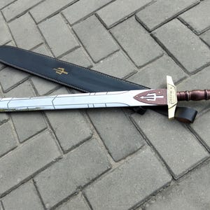 May include: A silver sword with a brown and gold handle, resting on a black sheath. The sword features a trident design on the blade and hilt. The sheath has a gold trident symbol.