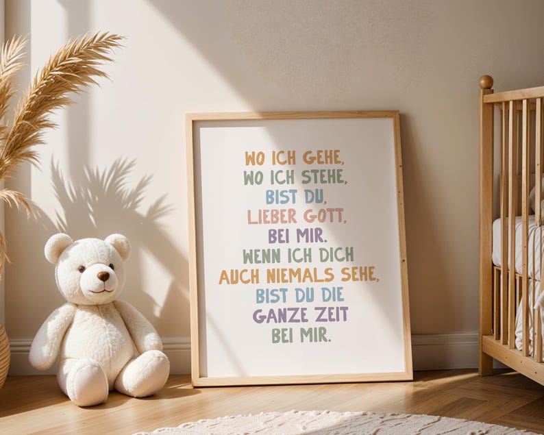 May include: A framed print with the text "WO ICH GEHE, WO ICH STEHE, BIST DU, LIEBER GOTT, BEI MIR." in various pastel colors. A white teddy bear and a wooden crib are in the background. The print is in a light-colored wooden frame.