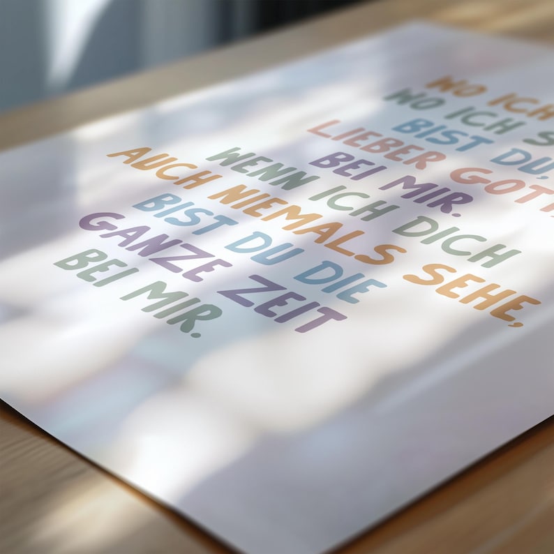 May include: A white poster with colorful text in German. The text includes phrases like "Lieber Gott bei mir" and "Ganze Zeit bei mir." The words are in various colors, including blue, orange, and green. The poster is on a wooden surface.