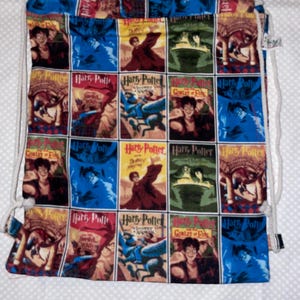 May include: A drawstring backpack featuring a repeating grid pattern of Harry Potter book cover illustrations in vibrant colors including blue, red, yellow, and green. The bag has white rope straps and displays various character scenes and the Harry Potter logo.