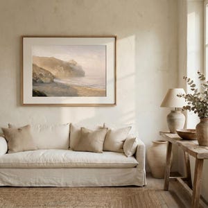 May include: A living room scene featuring a large framed landscape painting above a cream-colored sofa with beige pillows. A wooden side table holds a lamp, vase, and bowl. The room has a neutral color palette.