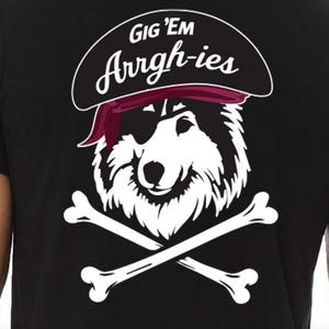 Puede incluir: Camiseta negra con una ilustración blanca de un perro pirata con sombrero y parche en el ojo, con huesos cruzados debajo. El texto "GIG 'EM Arrrgh-ies" está encima del perro. El diseño está centrado en la camiseta.