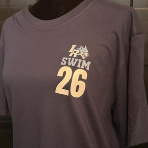 Peut inclure: T-shirt bleu marine avec un motif de t&ecirc;te de loup et le texte "LR SWIM 26" en blanc. Le t-shirt est pr&eacute;sent&eacute; sur un mannequin. Le t-shirt est fait d'une mati&egrave;re douce.