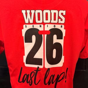 Peut inclure: T-shirt rouge avec l'inscription "WOODS SENIOR 26 Last lap!" en blanc et noir. Le chiffre 26 est grand et mis en &eacute;vidence, avec un bord blanc. Le t-shirt est en mati&egrave;re souple.
