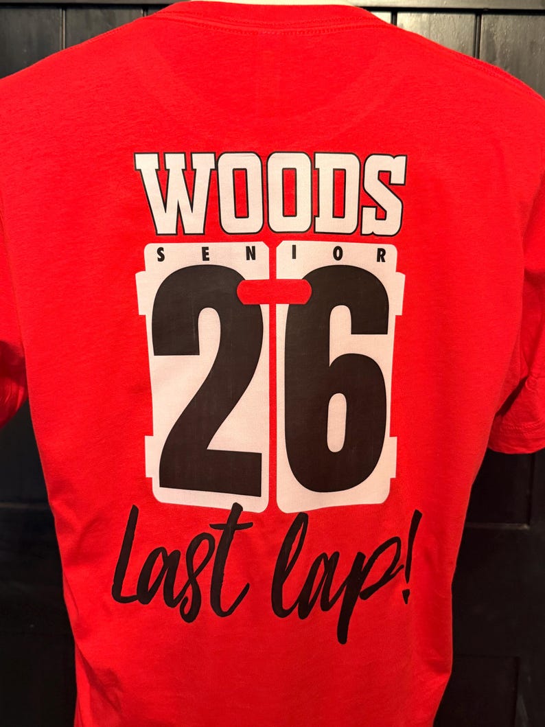 Peut inclure: T-shirt rouge avec l'inscription "WOODS SENIOR 26 Last lap!" en blanc et noir. Le chiffre 26 est grand et mis en &eacute;vidence, avec un bord blanc. Le t-shirt est en mati&egrave;re souple.