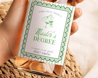 May include: A clear glass bottle filled with a light pink liquid, held by a hand. The bottle has a label with the text "Pairs well with a Master's Degree" in green and white. The label also includes the text "Congrats to the grads! Janet Smith."