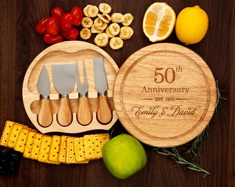 May include: A wooden cheese board set with four stainless steel cheese knives and a round cutting board engraved with "50th Anniversary" and the names "Emily & David." The image also includes crackers, fruit, and vegetables.