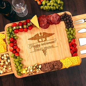 May include: A bamboo charcuterie board with the words "Happy retirement!" and a medical symbol engraved on it. The board is filled with grapes, strawberries, cheese, crackers, salami, and cookies. A wine bottle and glasses are in the background.