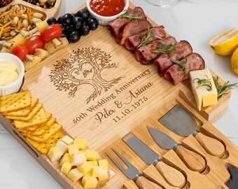 May include: A bamboo serving board with a tree design and the text "50th Wedding Anniversary Peter & Ariana 11.10.1975". The board is filled with crackers, cheese, meats, fruits, and dips. Includes cheese knives and forks.