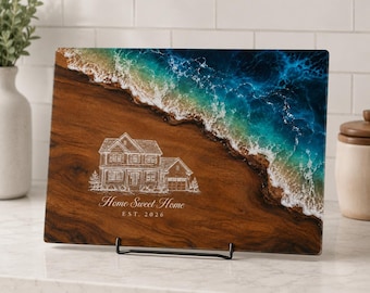 May include: A rectangular wooden serving board featuring a resin ocean design with blue and turquoise waves crashing against a brown wood grain shore. A white line drawing of a two-story house is engraved with the text Home Sweet Home EST. 2026.