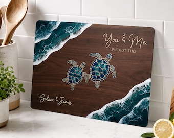 May include: A rectangular wooden cutting board featuring a dark brown wood grain finish, two sea turtles with blue and green shell patterns, and white ocean wave resin art on two corners. The text reads You & Me WE GOT THIS and Selena & James.