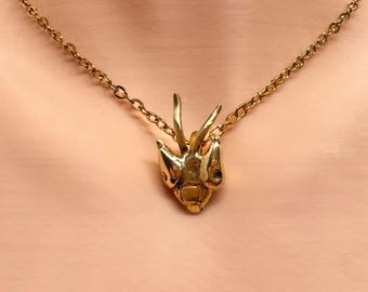 Pode incluir: Um colar dourado com um pingente em forma de cabeça de inseto. O pingente tem detalhes intrincados e é suspenso por uma corrente fina. O colar é exibido em um fundo neutro, destacando a joia.