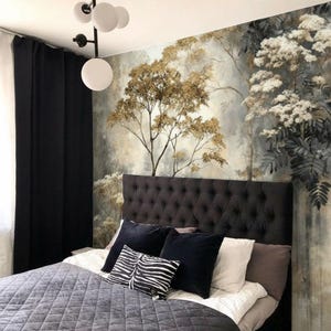 May include: A bedroom with a tufted headboard, a gray quilted bedspread, and decorative pillows. The wall features a mural of a forest scene with trees and foliage in shades of gold, gray, and white. Black curtains and a modern light fixture complete the room.