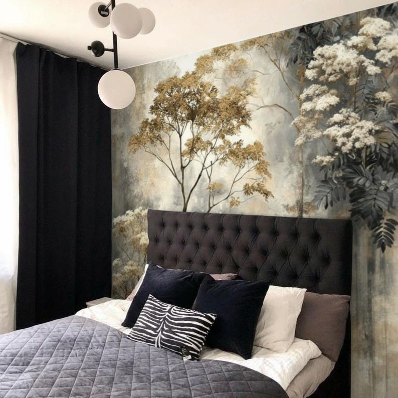 May include: A bedroom with a tufted headboard, a gray quilted bedspread, and decorative pillows. The wall features a mural of a forest scene with trees and foliage in shades of gold, gray, and white. Black curtains and a modern light fixture complete the room.