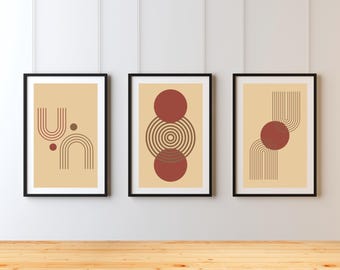 May include: Three framed abstract art prints. Each print features a beige background with geometric designs in shades of brown and red. The frames are black, and the prints are hanging on a white wall above a wooden surface.