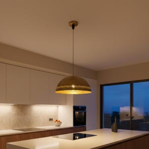 Puede incluir: Una l&aacute;mpara colgante con una pantalla en forma de c&uacute;pula de color dorado. La pantalla tiene un patr&oacute;n decorativo de peque&ntilde;os agujeros alrededor del borde inferior. La luz cuelga de un fino cable negro y est&aacute; montada en una l&aacute;mpara de techo de madera. La luz est&aacute; en una cocina.