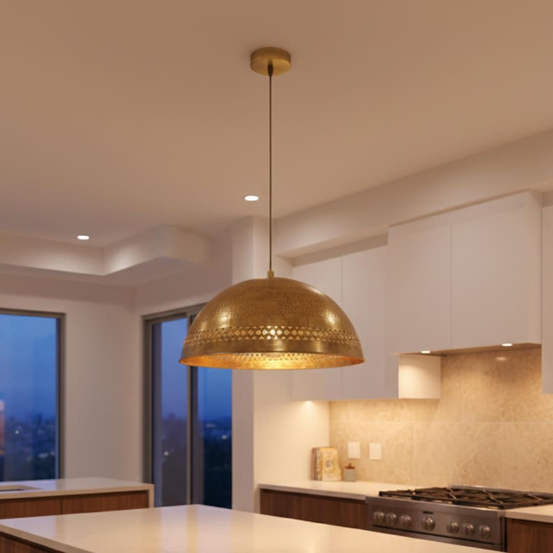 Puede incluir: Una l&aacute;mpara colgante dorada en forma de c&uacute;pula cuelga del techo. La luz tiene una superficie texturizada con un patr&oacute;n decorativo en el borde inferior. La l&aacute;mpara est&aacute; suspendida sobre una isla de cocina.