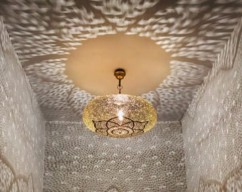 May include: A decorative, gold-colored, filigree pendant light fixture with a floral design. The light casts intricate patterns on the ceiling and walls, creating a warm and inviting ambiance. The fixture hangs from a brass-colored chain.
