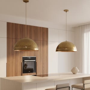 Puede incluir: Dos l&aacute;mparas colgantes de color lat&oacute;n con forma de c&uacute;pula cuelgan sobre una isla de cocina. Las luces tienen un dise&ntilde;o perforado alrededor del borde inferior. La cocina cuenta con una pared de acento de madera y un horno moderno.