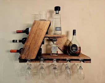May include: A wooden wine rack with a built-in glass holder. The rack holds three wine bottles, a shot glass, and several liquor bottles. The rack is made of dark brown wood and is mounted on a wall.