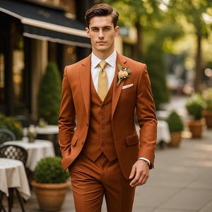 Könnte beinhalten: Ein dreiteiliger Anzug in Rostbraun, bestehend aus Blazer, Weste und Hose. Der Anzug wird mit einem weißen Hemd und einer goldenen Krawatte getragen. Eine florale Knopflochblume und ein Einstecktuch sind sichtbar. Der Mann geht auf einem Bürgersteig.