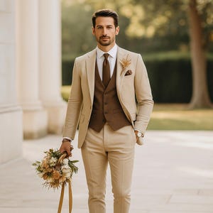 May include: A beige three-piece suit with a brown waistcoat and tie. The suit is paired with a white shirt and pocket square. The person is holding a bouquet of flowers.