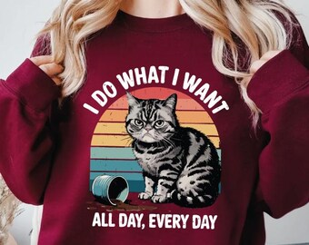 May include: Burgundy sweatshirt with a graphic of a gray tabby cat, a spilled can, and the text "I DO WHAT I WANT ALL DAY, EVERY DAY" in white. The cat is set against a retro sunset design.