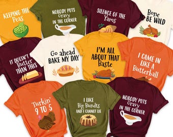 May include: A collection of colorful t-shirts with humorous Thanksgiving-themed phrases and graphics. The shirts are in various colors, including yellow, green, orange, and burgundy, with text like "Keeping the Peas" and "I'm All About That Baste."