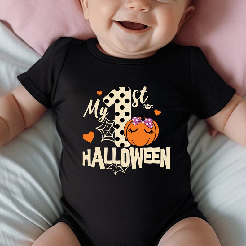 May include: A black short-sleeved baby bodysuit featuring a graphic with the text My 1st HALLOWEEN. The design includes a large polka-dot number one, an orange pumpkin with a purple polka-dot bow, spiderwebs, and small orange hearts.