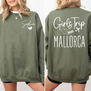 May include: Olive green sweatshirt with the name "Sophia" and a heart on the front. The back of the sweatshirt features the text "Girls Trip 2025 MALLORCA" with a heart and airplane graphic. A casual, comfortable garment.