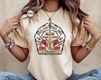 May include: A light yellow t-shirt with a graphic design featuring a guitar, skeleton hands, and the text "Rock and Roll Soul, Make Some Noise, Amazing Rock Festival". The design is in red, yellow, and black.