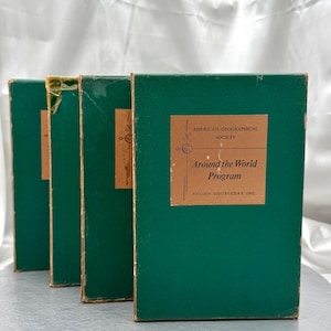 May include: Four green rectangular books standing upright in a row. Each book features a tan label on the front cover with the text American Geographical Society, Around the World Program, and Nelson Doubleday Inc. printed in black ink.