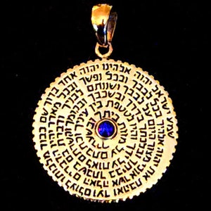 Puede incluir: Un colgante de oro con un diseño circular que presenta texto hebreo y una piedra preciosa azul en el centro. El colgante está sobre un fondo negro.