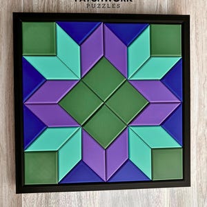 May include: A framed Patchwork Puzzles geometric design. The puzzle features a starburst pattern in shades of green, teal, purple, and blue. The puzzle is set in a black frame and is displayed on a wooden surface.