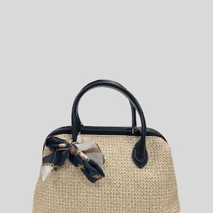 May include: A beige woven handbag with black leather handles and trim. A patterned scarf is tied to the handle. The bag has a structured shape and a classic design, suitable for everyday use.