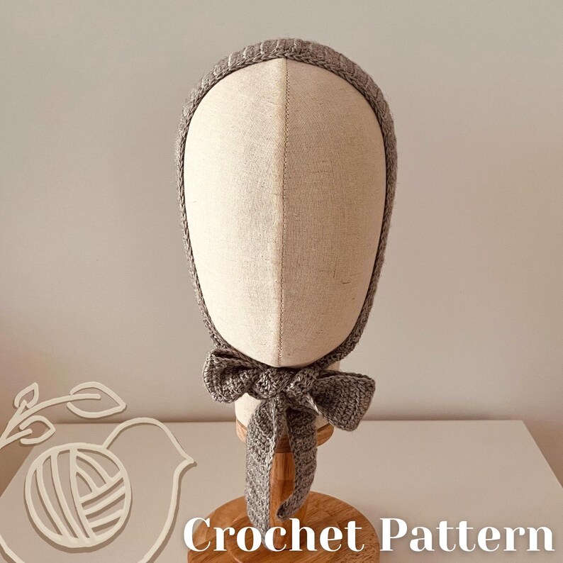 May include: A grey crochet bonnet with a bow, displayed on a mannequin head. The bonnet is made of a soft, textured yarn and features a delicate, ribbed trim. The words "Crochet Pattern" are at the bottom of the image.