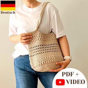 May include: A beige crochet tote bag featuring a textured bobble stitch pattern at the top and bottom, separated by a central section of openwork grid stitching. The bag has a single shoulder strap and is crafted from a neutral-colored yarn.