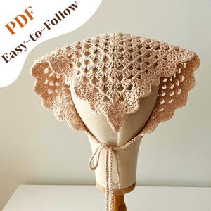 May include: A light peach-colored, crocheted sun hat with a scalloped edge and a tie closure. The hat is displayed on a mannequin head. The text "PDF Easy-to-Follow" is in the upper left corner.