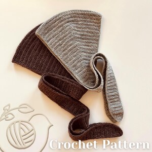 May include: A crochet pattern showing two triangular pieces and two long, narrow strips of crocheted fabric in shades of brown and grey. The text "Crochet Pattern" is at the bottom. The items are arranged on a light-coloured surface.