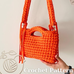 May include: A bright orange crochet handbag featuring a rectangular body with a cutout handle, a thick braided shoulder strap, and long fringe accents on the sides. The text "Crochet Pattern" is visible in the lower portion of the image.