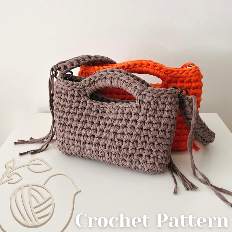 May include: Two rectangular crochet handbags with integrated handles, one in a muted taupe and one in a vibrant orange. The taupe bag features long, thin fabric fringe accents on the sides. The image includes a logo and the text Crochet Pattern.