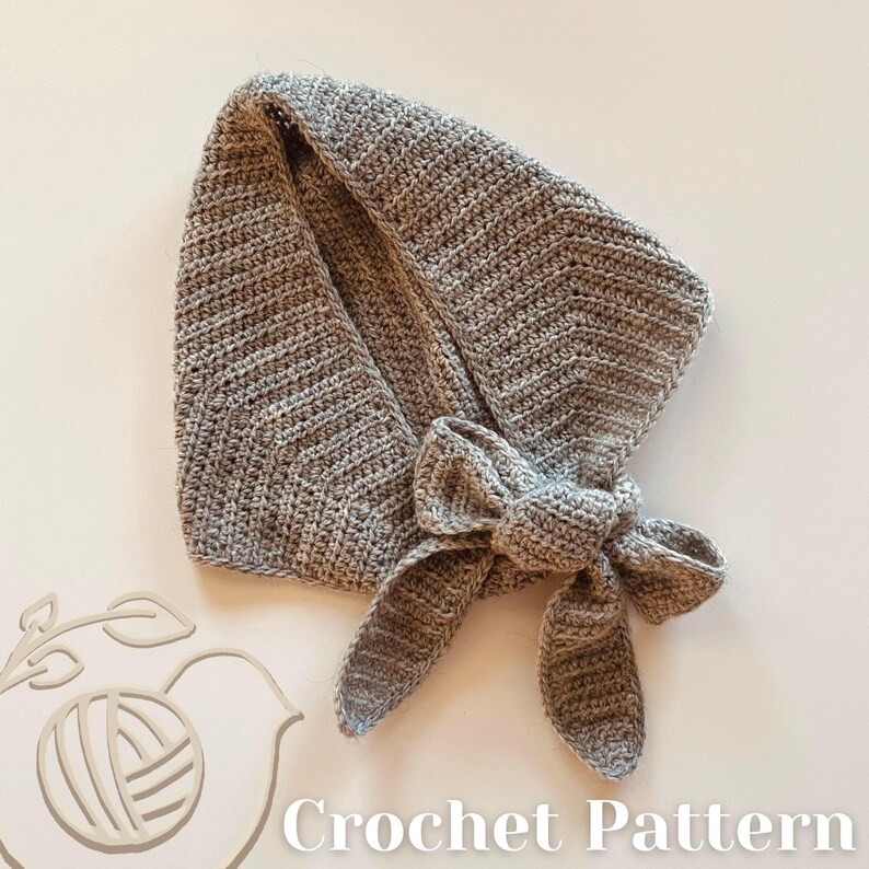 May include: A grey crocheted scarf with a bow. The scarf is made from a soft, textured yarn and is folded over. The words "Crochet Pattern" are visible at the bottom of the image.