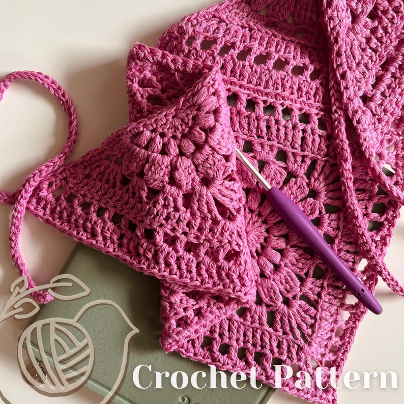 Puede incluir: Primer plano de un patr&oacute;n de crochet rosa con un gancho de crochet. El patr&oacute;n es un cuadrado con un dise&ntilde;o de flor en el centro. El texto "Crochet Pattern" es visible en la parte inferior de la imagen.