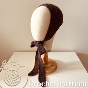 May include: A dark brown crochet bonnet with long ties, displayed on a mannequin head. The bonnet is made of a textured yarn and features a bow at the front. The text "Crochet Pattern" is visible at the bottom of the image.