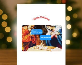 Puede incluir: Una tarjeta de Navidad blanca con el texto "Merry Christmas" en escritura roja. La tarjeta presenta una imagen humorística de la escena de la Natividad con bocadillos que dicen "Should we livestream this?" y "just post a reel". La tarjeta tiene el texto "C'est Cadeau Co".