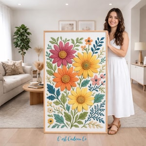 May include: A framed floral art print featuring large, textured flowers in shades of pink, orange, and yellow, with green and blue foliage. The artwork is displayed in a light-colored wooden frame. The text "C'est Cadeau Co" is visible at the bottom.