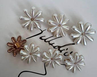 May include: A set of seven white pearl flower buttons with gold centers. The buttons are arranged in a semi-circle on a white surface.